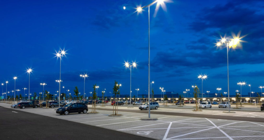 Expansive parking area at dusk illuminated by high-mounted LED floodlights on tall masts