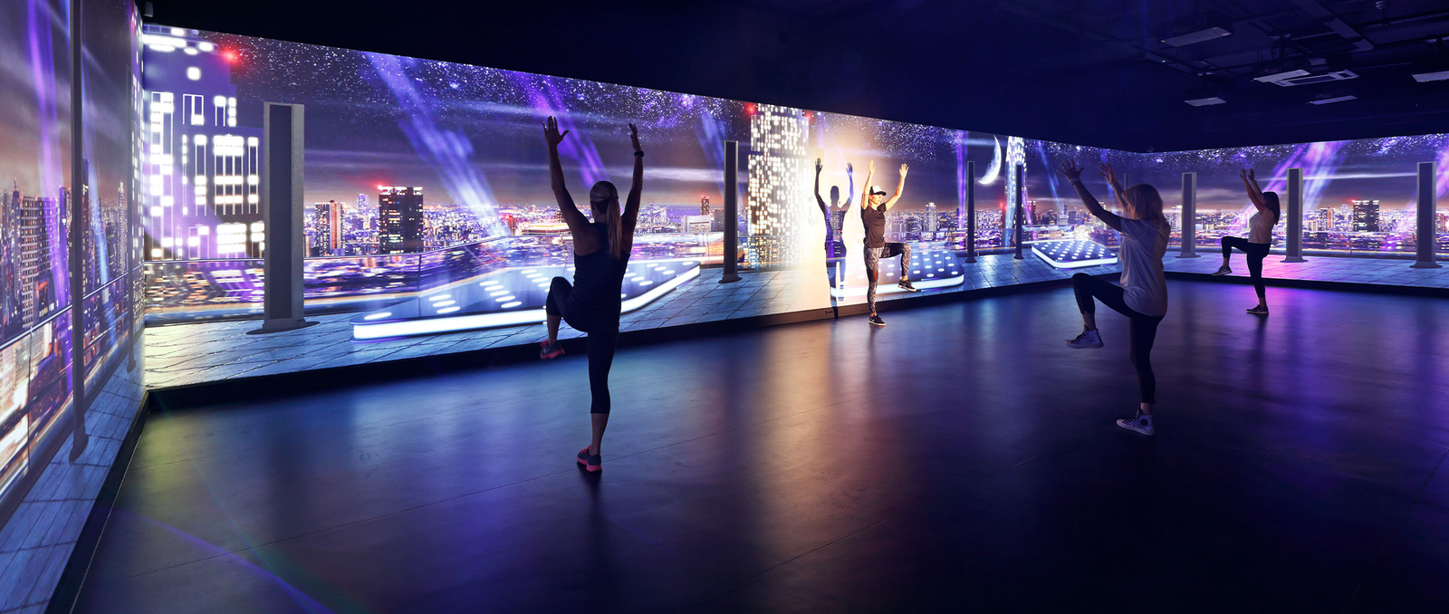 Group fitness studio with people doing yoga poses in front of an immersive LED wall showing a city skyline backdrop