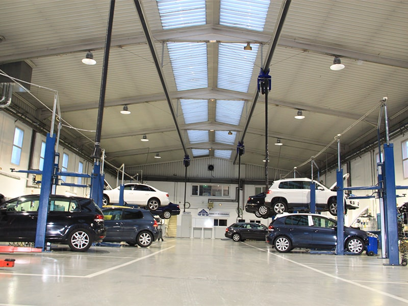 Volkswagen workshop service bay with multiple cars on lifts, ceiling lights and bright industrial lighting
