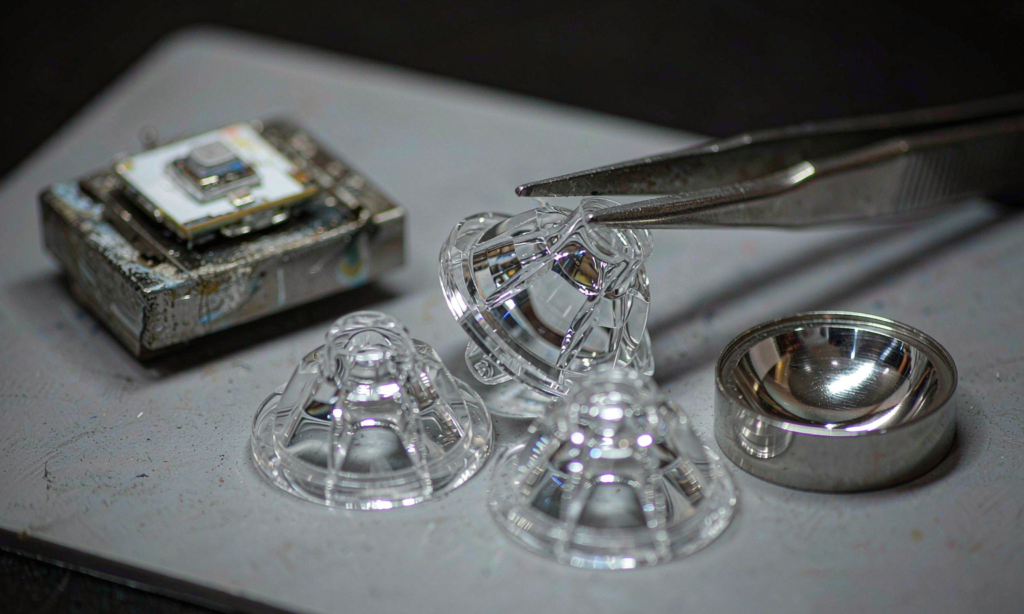 Optical engineer inspecting clear injection moulded LED lenses and a polished steel mould insert on a workbench