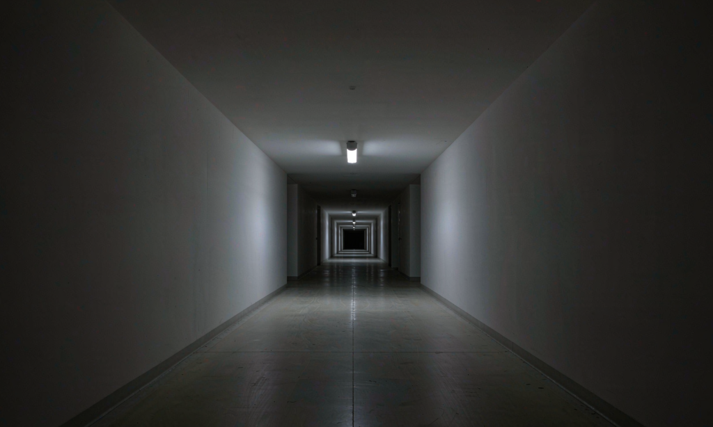 Ceiling-mounted emergency luminaire lighting a dark commercial corridor