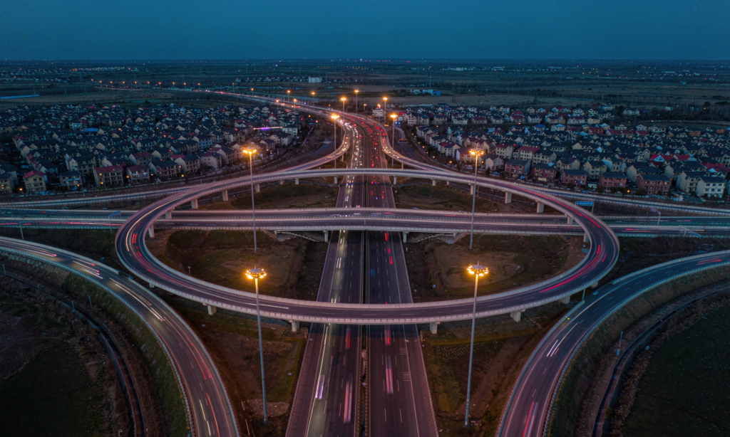 Aerial view of a highway interchange at dusk illuminated by tall high-mast LED lighting poles